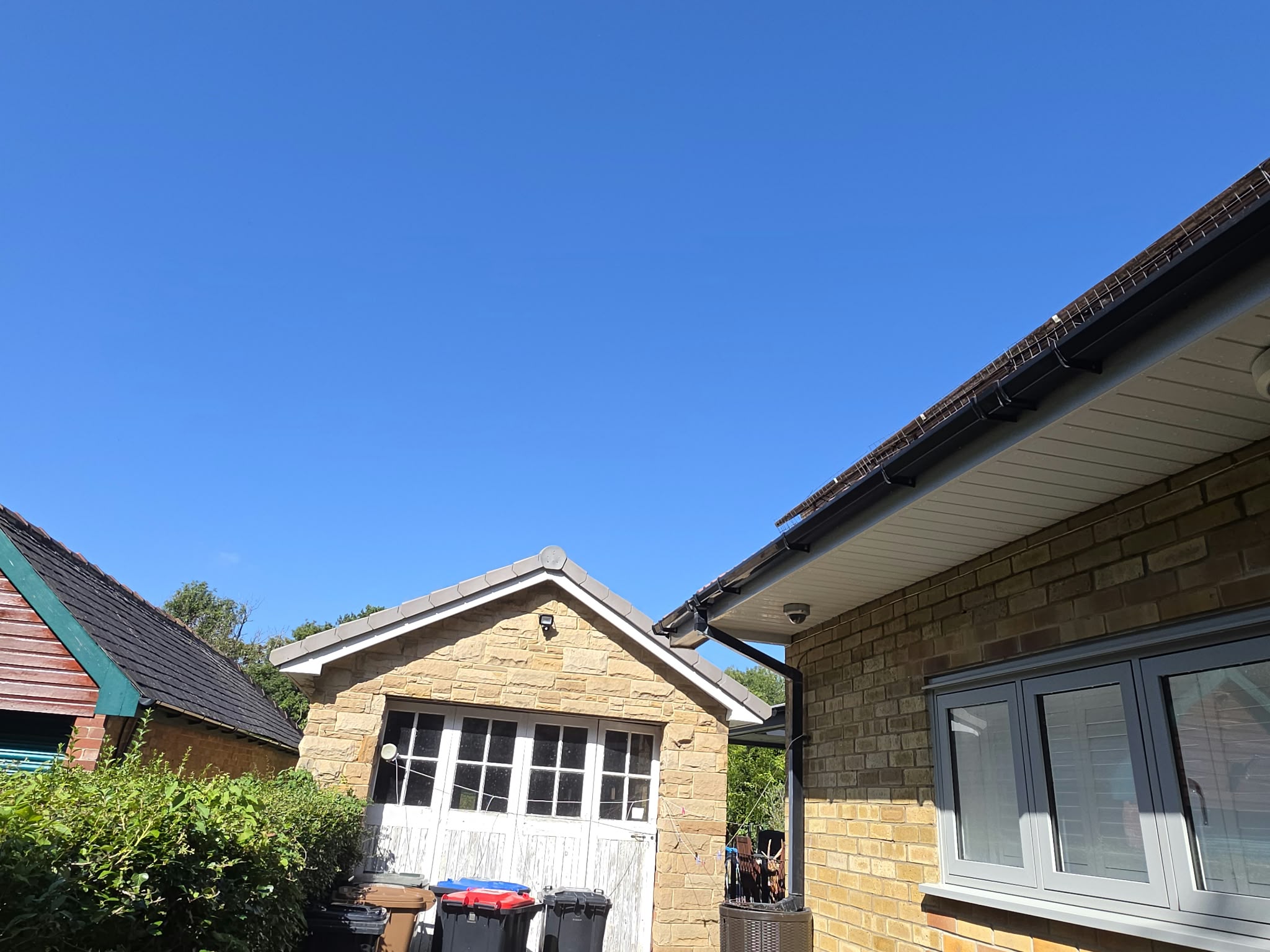 White soffit and a black external gutter beside a stone garage